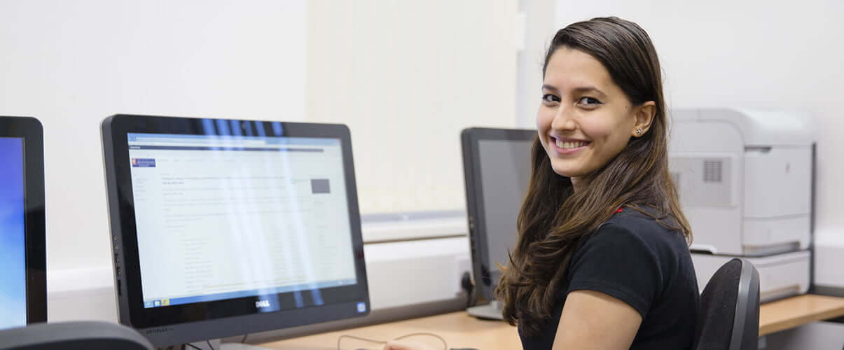Student smiling to camera whilst working at computer