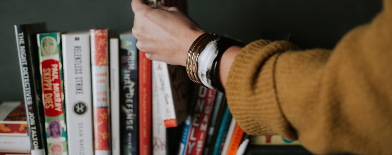 Person picking out book from bookshelf