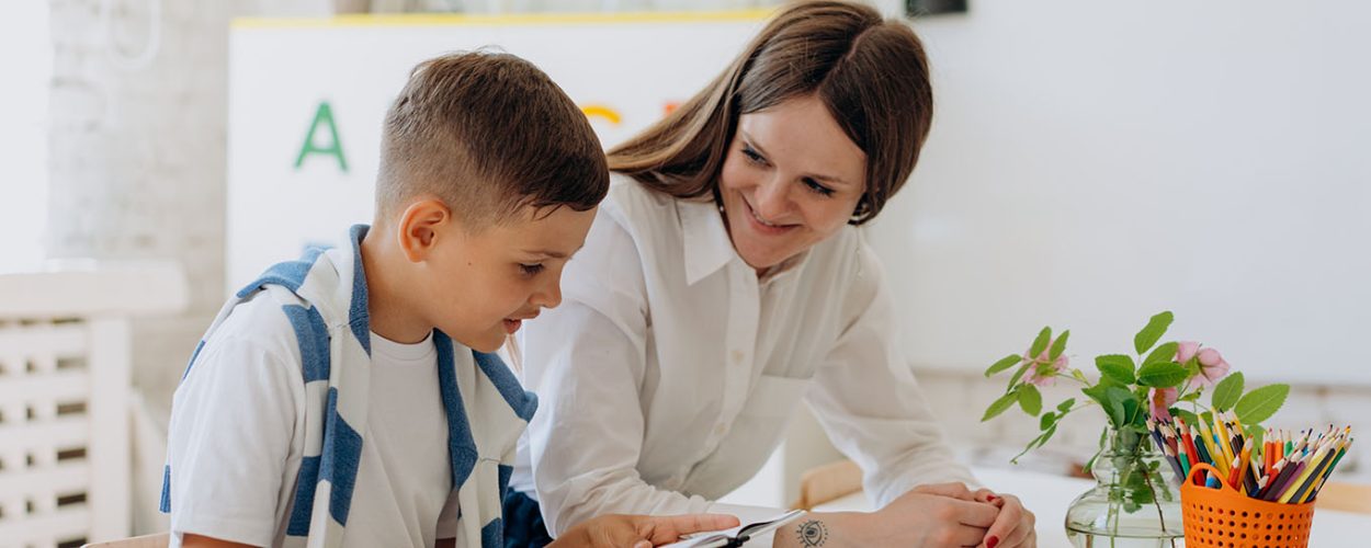 Teacher helping primary school aged pupil in classroom