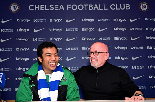 Prince and Paul smiling and laughing, with Chelsea Football Club press conference-style background
