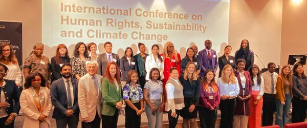 Guests standing on the stage of the auditorium with 'International Conference on Human Rights, Sustainability and Climate Change' wording on the screen behind.