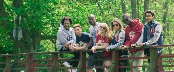 Group of Buckingham students smiling to camera, standing on bridge over river