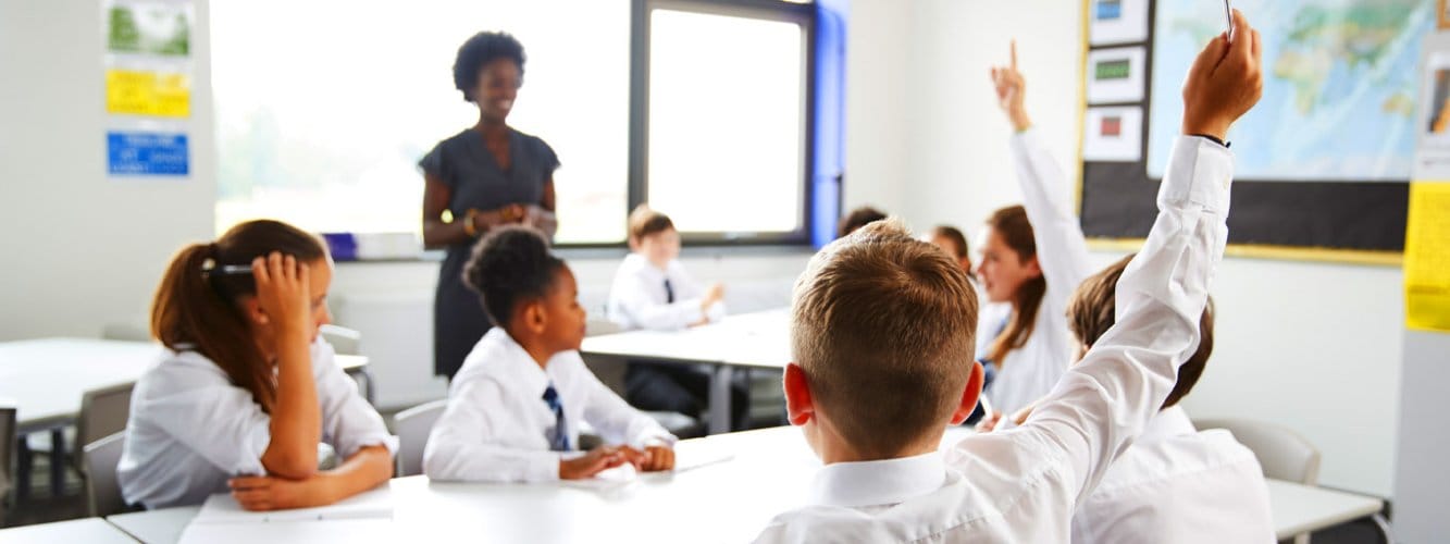 Students with hands up in secondary school classroom
