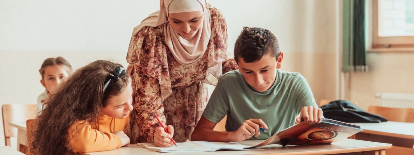 Female teacher between two young students helping with work