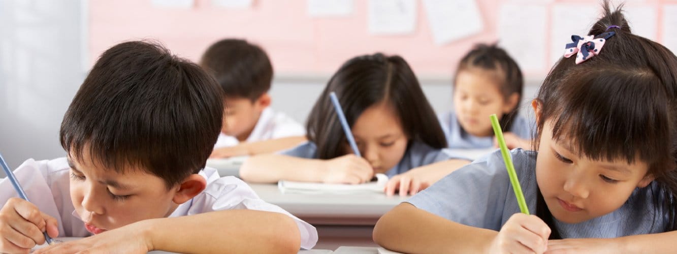 Primary school pupils in classroom, writing on paper at desks
