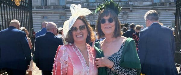 Sarah Myhill and Patricia Covarrubia smiling to camera, standing outside the front of Buckingham Palace