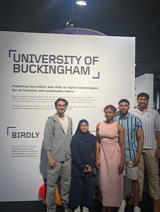 Buckingham students at the Goodwood Festival of Speed, next to large sign with write-up about the University.