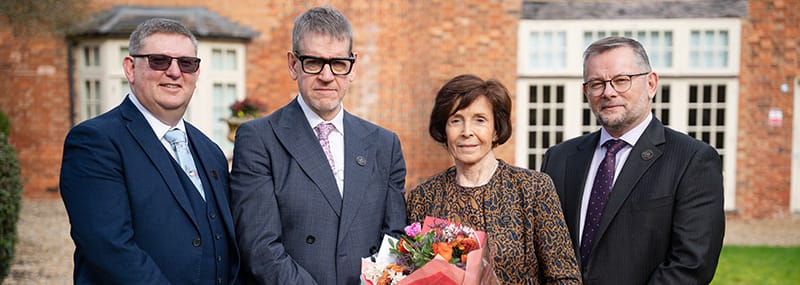 Left to right: Chris Payne, Mark Qualter, Dame Mary Archer and David Cole. Dame Mary is holding a bunch of gifted flowers, all standing in The University of Buckingham grounds.