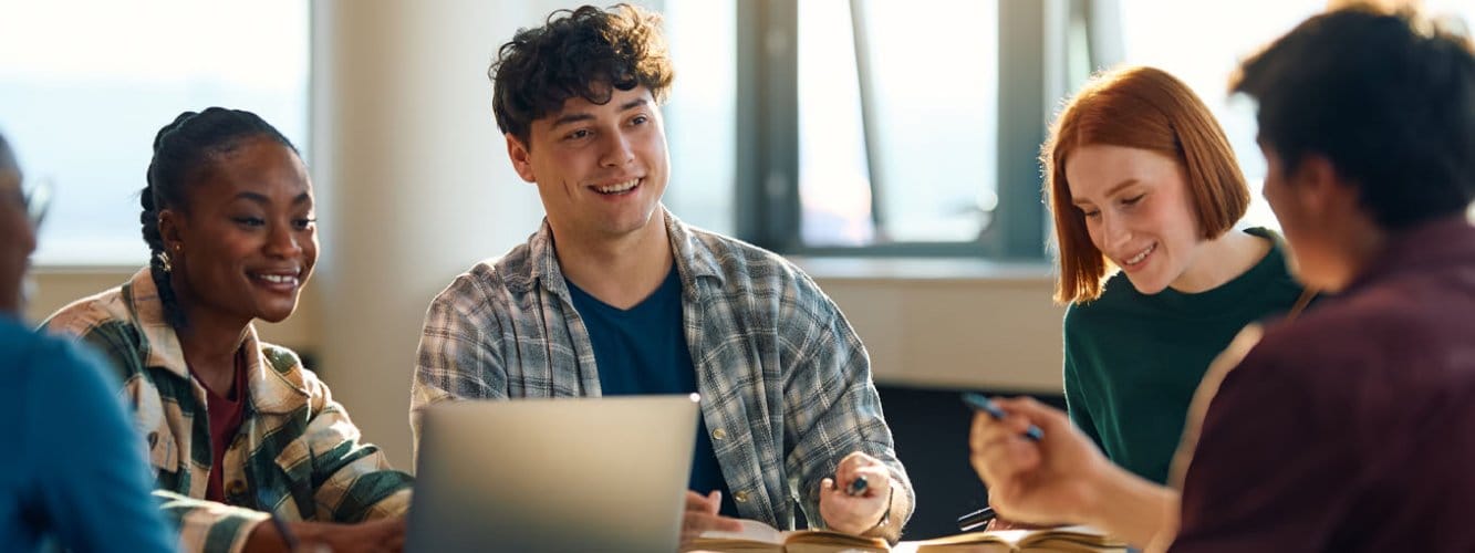 Group of university students talking around desk, with books and laptop