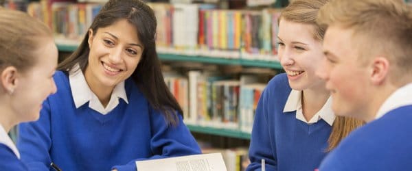 Group of four secondary school pupils sitting around table in library, working together